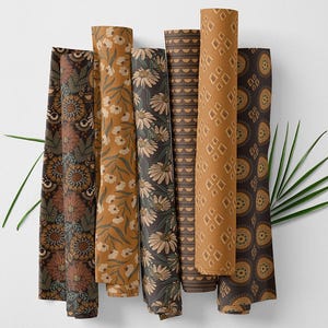 Op de afbeelding: Gerolde stoffen rollen met diverse bloemen- en geometrische patronen. Het kleurenpalet omvat bruin-, goud- en grijstinten. Sommige rollen tonen madeliefjes- en zonnebloempatronen, andere ruit- en cirkelmotieven.