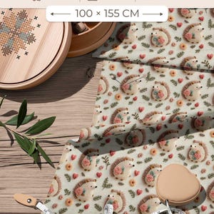 Peut inclure: Un tissu en satin 100% coton avec un motif répétitif de hérissons, de roses roses et de petits cœurs sur fond crème. Le tissu mesure 100 x 155 cm, pèse 140 GSM et est fabriqué en Turquie. Un ruban à mesurer est visible sur le tissu.