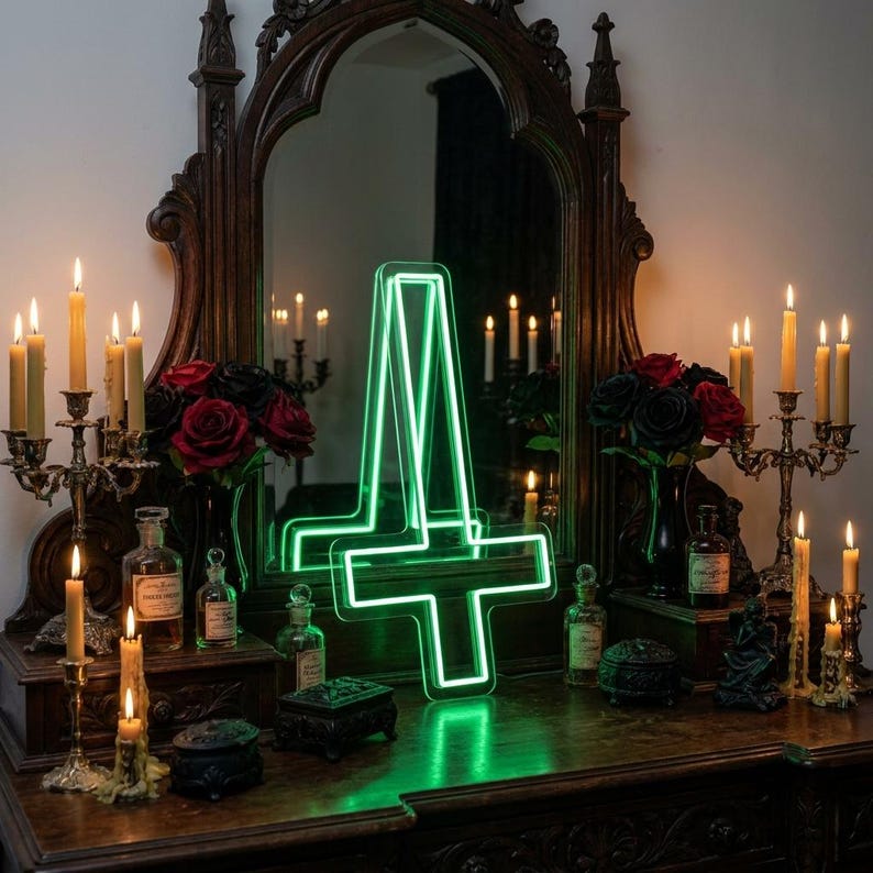 May include: A green neon inverted cross sign is displayed on a dark wooden surface, reflecting in a large ornate mirror. The scene is decorated with lit candles, red and black roses, and antique bottles, creating a gothic aesthetic.