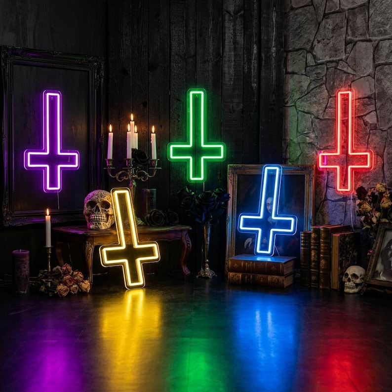 May include: A collection of neon inverted crosses in purple, green, yellow, blue, and red. The crosses are illuminated and placed on a dark surface with gothic decor, including candles, skulls, and antique frames. The crosses are a unique decorative item.