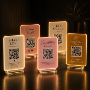 Könnte beinhalten: Eine Sammlung beleuchteter Acrylschilder mit verschiedenen Texten und QR-Codes. Die Schilder sind in Weiß-, Rosa- und Goldtönen gehalten und tragen Aufschriften wie "Share Love", "Cheers Tonight" und "Consultation Booking". Jedes Schild hat einen transparenten Sockel.