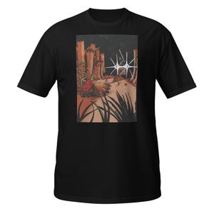 May include: Black t-shirt featuring a detailed graphic print. The artwork depicts a surreal landscape with stylized trees, a central star-like structure, and plant life. The color palette includes shades of brown, green, and white.