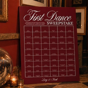 以下が含まれることがあります： First Dance Sweepstakeと白文字で書かれた長方形のバーガンディ色の看板。ゲストが署名するための曲名とアーティスト名のグリッドが特徴です。下部には筆記体でLucy & Noahという名前が記されています。