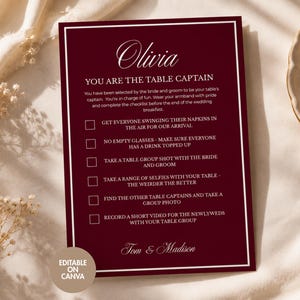 May include: A rectangular burgundy wedding table captain card with white text and a double-line border. The card features the name Olivia, the title You Are The Table Captain, and a checklist of six tasks for wedding guests, ending with Tom & Madison.