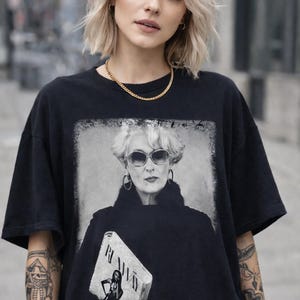 Könnte beinhalten: Schwarzes T-Shirt mit einem Schwarz-Weiß-Bild einer Frau mit Sonnenbrille und Pelzkragen. Das Bild auf dem Shirt enthält das Wort "RUNWAY". Eine goldene Halskette ist ebenfalls zu sehen.