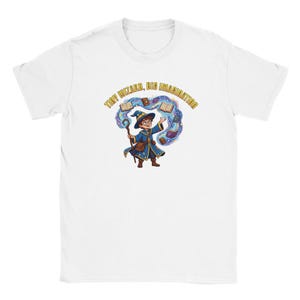 Puede incluir: Camiseta blanca con un mago de dibujos animados con una túnica azul, sosteniendo un bastón y rodeado de libros flotantes. El texto "TINY WIZARD, BIG IMAGINATION" está arqueado sobre el mago en letras amarillas.
