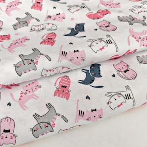 Può includere: Tessuto bianco con un motivo ripetuto di gatti dei cartoni animati in rosa, grigio e nero. I gatti sono in varie pose, alcuni con fiocchi, su uno sfondo bianco. Il tessuto è piegato, mostrando la continuità del motivo.