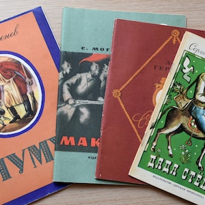 May include: Four vintage books with illustrated covers. The leftmost book is orange with a circular illustration of a person and a dog. The second is green with black text. The third is dark red with gold patterns. The rightmost is green with a person riding a donkey.