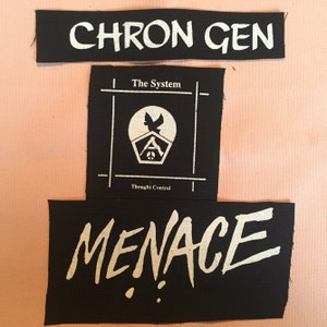 Pode incluir: Três patches de tecido preto com texto e gráficos brancos. O patch superior diz "CHRON GEN". O patch do meio apresenta um gráfico com as palavras "The System" e "Thought Control". O patch inferior diz "MENACE".