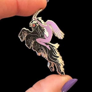 May include: A silver-toned pin featuring a mythical creature with a black body and a lavender-colored figure riding it. The figure has red eyes and is holding a curved object. The pin has a black background.