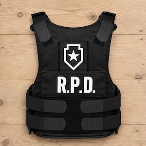 Puede incluir: Un chaleco táctico negro con un logotipo R.P.D. blanco en el pecho y un emblema de estrella blanca dentro de una forma de escudo sobre el texto. El chaleco incluye correas ajustables para los hombros y dos correas laterales con velcro.