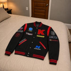 May include: A black varsity jacket featuring red accents on the collar, cuffs, hem, and pocket trim. The front displays various embroidered patches including the text K, CAMEO, Trigger, RENEGADE, HORIZON, ZONBE, and GOODBYE, along with other graphic logos.