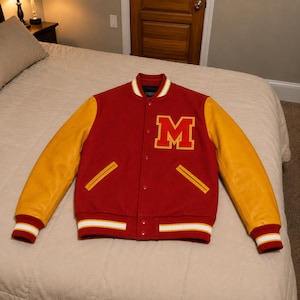 May include: A red varsity jacket with yellow sleeves, featuring a large yellow letter M with a red outline on the left chest. The jacket has a snap-button front closure, two side pockets, and ribbed cuffs and hem with white and yellow stripes.