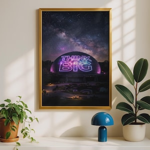 Könnte beinhalten: Ein rechteckiger Wandkunstdruck in einem goldenen Rahmen, der eine große Kuppelstruktur bei Nacht unter einem sternenklaren Nachthimmel zeigt. Die Kuppel ist mit leuchtendem violett-weißem Neontext beleuchtet, der THINK BIG lautet.