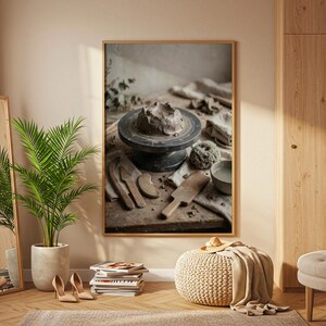 May include: A framed wall art print featuring a pottery wheel with a lump of gray clay, surrounded by wooden sculpting tools, a small bowl of water, and a textured sponge on a rustic wooden table, captured in a neutral-toned interior room.