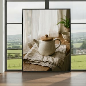 May include: A speckled ceramic teapot with a wooden lid rests on a folded linen cloth. The teapot is placed near a window with a view of a green countryside. The scene evokes a sense of calm.