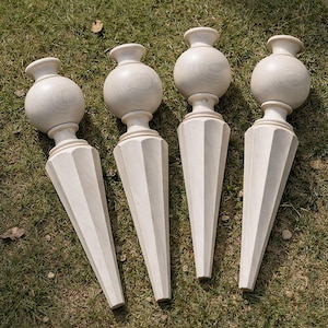 May include: Four unfinished wooden furniture legs. Each leg features a rounded top, a bulbous midsection, and a faceted, tapered base. The legs are light-colored and appear to be made of a hardwood.