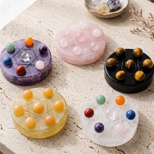 May include: Five circular stone discs, each featuring a carved six-pointed star pattern on the surface. The discs are crafted from purple amethyst, pink rose quartz, black obsidian, yellow citrine, and clear quartz, each topped with small gemstone spheres.