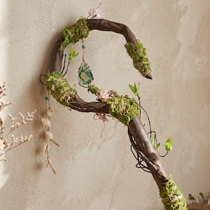 May include: A handcrafted wooden staff with a curved top, adorned with green moss, small pink flowers, and a hanging green crystal. The staff has a natural, rustic appearance, with vines and small leaves adding to its enchanted aesthetic.