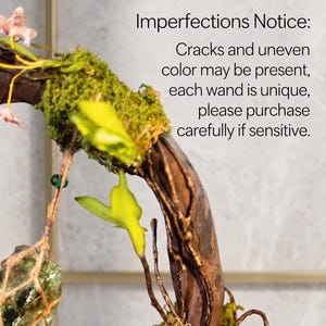 May include: A close-up of a decorative wand with a wooden branch base, adorned with green moss, yellow leaves, and small pink flowers. The wand has a natural, rustic appearance. Text on the image reads: "Imperfections Notice: Cracks and uneven color may be present..."
