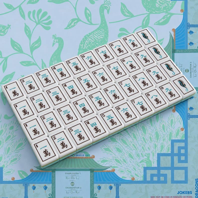Pode incluir: Um conjunto de pe&ccedil;as retangulares brancas de mahjong dispostas em uma grade, com caracteres chineses pretos para os n&uacute;meros de um a nove, alguns em azul. As pe&ccedil;as incluem ilustra&ccedil;&otilde;es de cavalos-marinhos nas extremidades.
