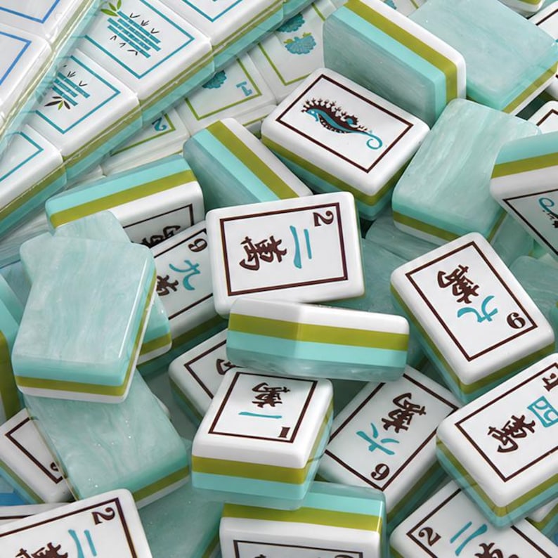 Pode incluir: Uma cole&ccedil;&atilde;o de pe&ccedil;as retangulares de mahjong com face branca, caracteres chineses em preto e azul-petr&oacute;leo, n&uacute;meros e ilustra&ccedil;&otilde;es de um cavalo-marinho e bambu. As pe&ccedil;as t&ecirc;m um verso em azul claro marmorizado e bordas verdes.
