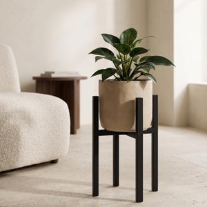 Op de afbeelding: Een groene Philodendron Birkin plant met bonte bladeren in een matte beige cilindrische keramische pot, geplaatst op een zwarte metalen plantenstandaard met vier verticale poten en een kruisvormige ondersteuningsstructuur.