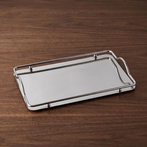 Könnte beinhalten: Ein rechteckiges Tablett aus silberfarbenem Metall mit einer polierten, reflektierenden Oberfläche. Das Tablett verfügt über eine erhöhte Reling entlang des Randes, die von kleinen kugelförmigen Elementen gestützt wird, sowie integrierte Griffe an den kurzen Seiten.
