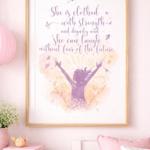 May include: A framed print with a light wood frame. The artwork features a purple silhouette of a person with arms raised, surrounded by floral and butterfly accents. The text reads, "She is clothed with strength and dignity and she can laugh without fear of the future."
