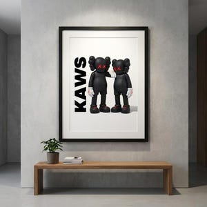 May include: Framed art print featuring two black figures with red 'X' eyes and hands, and red shoes. The word 'KAWS' is printed vertically in black. The artwork is displayed above a wooden bench with a small plant.