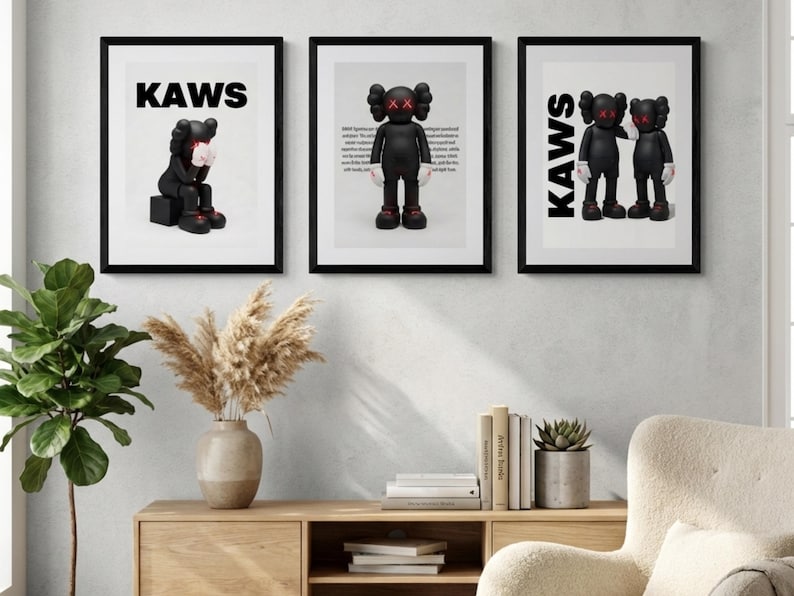 May include: Three framed art prints featuring black KAWS figures with red X eyes. The prints have the word "KAWS" in bold black letters at the top. The figures are in different poses, set against a white background.