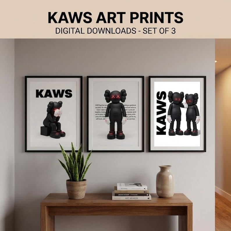 May include: Three framed KAWS art prints. Each print features a black KAWS figure with white gloves and red X eyes. The prints are displayed on a wooden table with a plant and a vase. The text "KAWS ART PRINTS" is at the top.