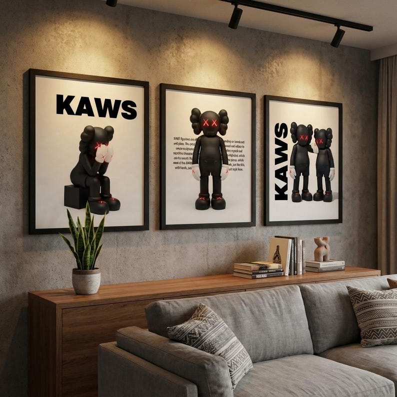 May include: Three framed KAWS art prints hang above a wooden cabinet and gray sofa. Each print features a black figure with red X eyes and white gloves. The word "KAWS" is printed in bold black letters on two of the prints.