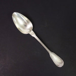 May include: A silver spoon with a rounded bowl and a long, slender handle. The handle has a decorative design with a heart-shaped motif at the end.