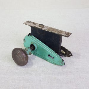 May include: Antique door hardware with a teal green plate, a round brass knob, and a keyhole. The hardware is in a worn condition.
