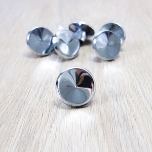 May include: A collection of shiny, silver-colored cabinet knobs with a rounded, faceted design. The knobs are arranged on a light-colored wooden surface, reflecting the surrounding light. These decorative knobs are suitable for furniture and home decor projects.