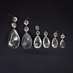 May include: A set of seven clear glass crystal teardrop pendants of varying sizes. The pendants are strung on silver wire and have a faceted design.
