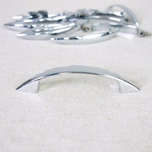 May include: A collection of polished chrome cabinet pulls with a curved, arching design. Each handle features a smooth, reflective metallic finish and tapered ends with visible screw holes on the underside for mounting to furniture or cabinetry.