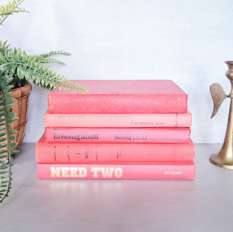May include: A stack of five pink books with different titles. The top book is titled "NEED TWO" in yellow letters. The second book is titled "Investigation" and the third book is titled "The Man Who Laughed at Murder".