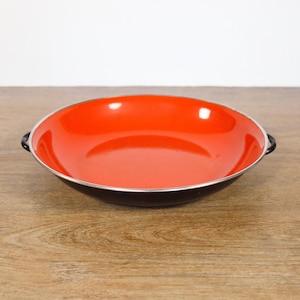 May include: A black and orange enamelware bowl with two handles. The bowl is empty and sitting on a wooden surface.