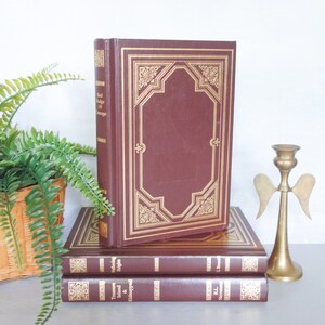 May include: A stack of three hardcover books with gold accents. The top book is titled "Red Badge of Courage" and the bottom book is titled "Treasure Island & Kidnapped".