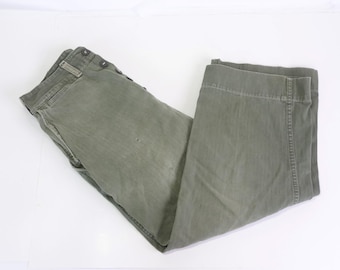May include: A pair of green utility pants with a button fly and multiple pockets. The pants are folded in half and have a worn, vintage look.
