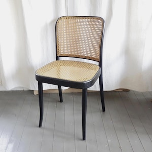 May include: A black wooden chair with a woven cane seat and back. The chair has a rectangular seat and a curved backrest. The legs are slightly curved. The chair is a classic design, suitable for a dining room or living room.