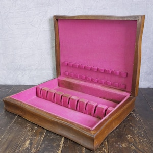 May include: Open wooden silverware box with a bright pink felt interior. The box is rectangular with a hinged lid and compartments for storing utensils. The exterior is a warm brown color, and the interior is a vibrant pink.