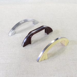 May include: Three vintage cabinet pulls in silver, brown, and cream. The silver pull has a ribbed design, while the brown and cream pulls have a silver accent. These decorative handles are ideal for adding a retro touch to furniture.