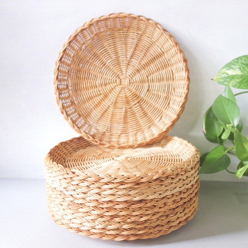 May include: A stack of round, light brown woven wicker baskets. The top basket is positioned vertically, displaying a circular, radiating weave pattern, while the base consists of several stacked baskets with a horizontal, braided side weave.