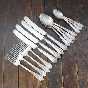 May include: An assortment of vintage silverware, including forks, knives, and spoons, arranged on a dark wooden surface. The silverware has ornate handles and a shiny, reflective finish, suggesting a classic or antique style.