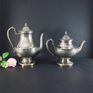 May include: A silver tea set with a larger teapot and a smaller creamer. Both pieces have a fluted design and a shiny finish.