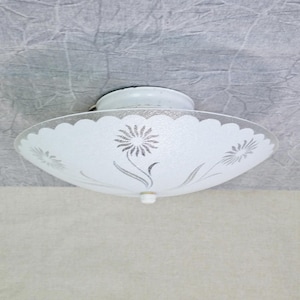 May include: A white, scalloped-edge ceiling light fixture with a frosted glass shade. The shade features a floral design in gray and is attached to a white base. The fixture is designed for ceiling mounting.