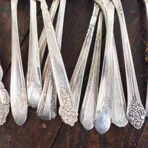 May include: A collection of vintage silver teaspoons with ornate handles. The spoons have a polished finish and intricate floral designs.